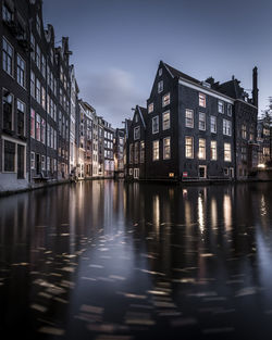 Illuminated buildings by river against sky in city