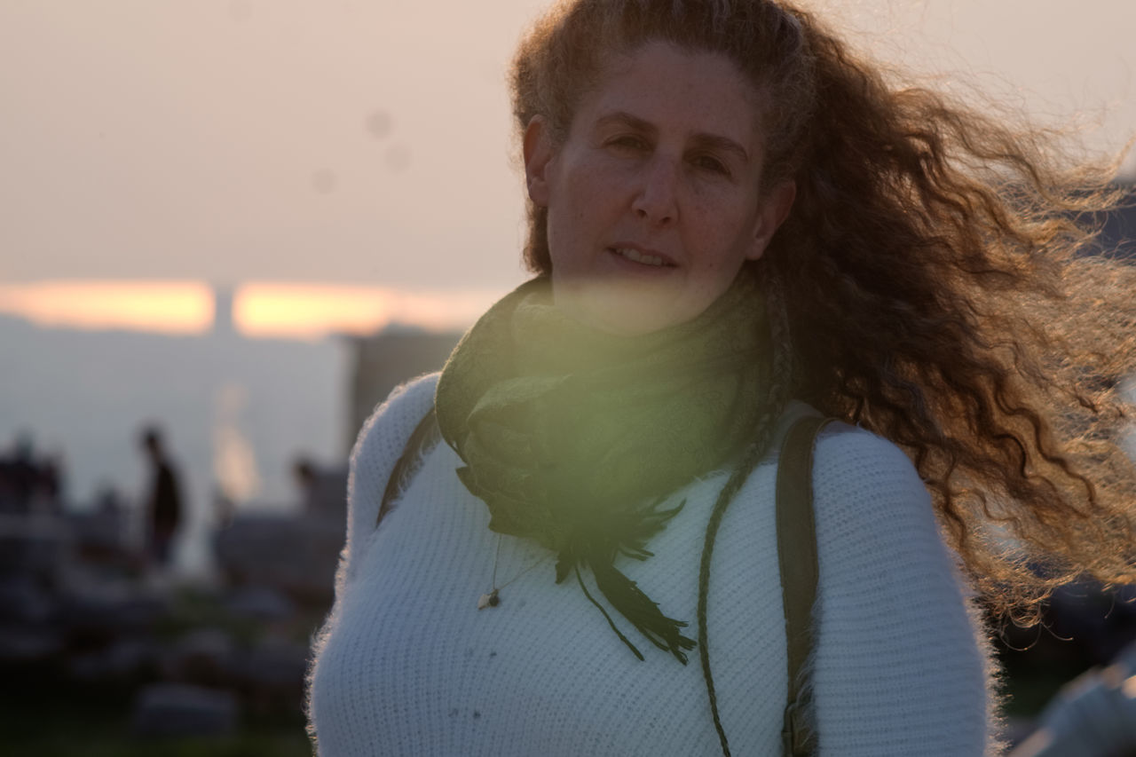 PORTRAIT OF YOUNG WOMAN STANDING ON BEACH DURING SUNSET