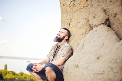 Young man on rock against sky