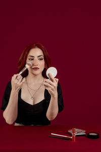 Portrait of young woman drinking glass against yellow background