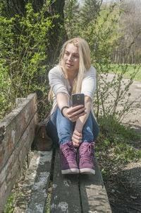 Young woman using phone while sitting on tree