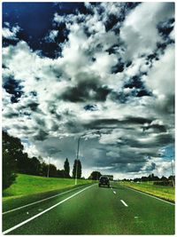 Road passing through field against cloudy sky