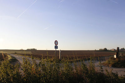 Road sign on field against clear sky