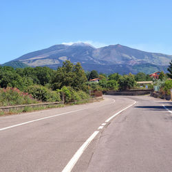 Empty road along trees and mountains against sky