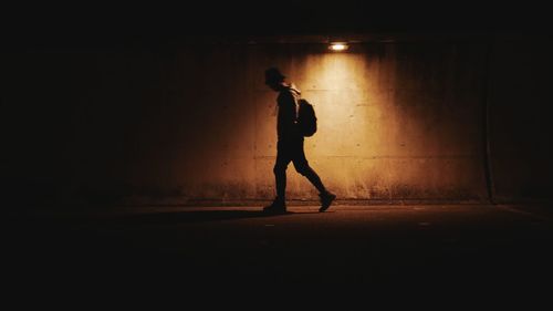 Man walking on road by illuminated wall