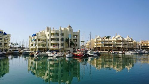 Sailboats moored on river by buildings against sky