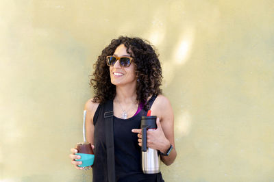 Mixed race woman smiling while drinking mate outdoors.