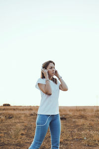 Young women looking away while standing on field against sky