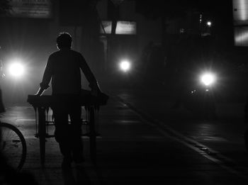 Full length rear view of vendor with push cart walking on street at night