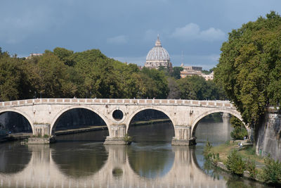 Arch bridge over river by buildings against sky