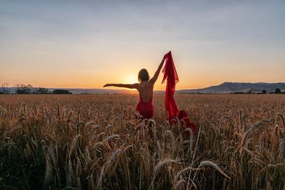 Woman standing on field against sky during sunset