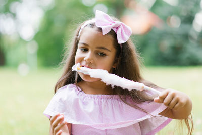 Cute baby girl in pink dress eats white cotton candy in the park in summer