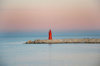 Lighthouse by sea against sky during sunset