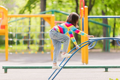 A girl in a bright striped jumper and jeans, climbs the childrens stairs on the playground