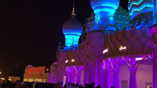 People in illuminated building against sky at night