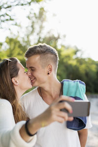 Romantic couple taking self portrait while kissing outdoors