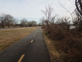 Empty road along bare trees against sky