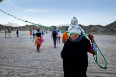 Rear view of person carrying child on shoulder and holding rope while standing outdoors