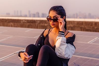 Portrait of young woman sitting on retaining wall against sky