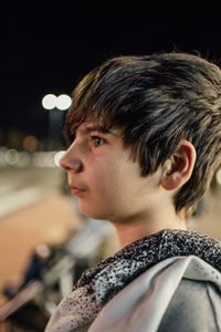 Portrait of caucasian teenager boy at night in the street with burning lights in the background