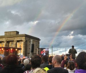 People on rainbow in city against sky