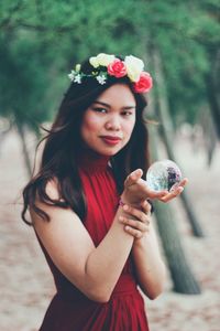 Portrait of beautiful woman holding red while standing against plants