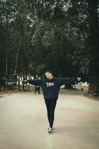 Full length portrait of young woman standing against trees