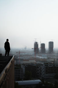 Rear view of man looking at cityscape against clear sky