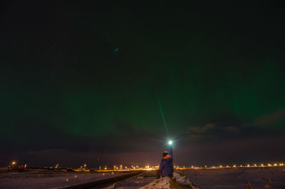 Man on illuminated street light against sky at night