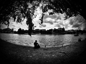 Silhouette people sitting on riverbank against sky