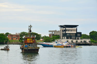 Boats sailing on river by buildings against sky