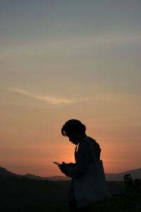 Side view of silhouette man using smart phone against sky during sunset