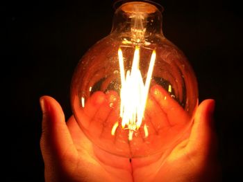 Close-up of hand holding illuminated candle against black background