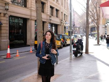 Full length of young woman using phone on city street