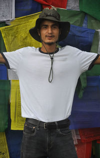 Portrait of young man wearing hat standing against prayer flag