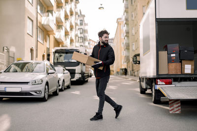 Young delivery man carrying box while walking on street in city