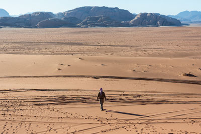 Full length rear view of man walking on desert