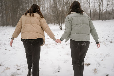 Rear view of young women standing on snow outdoors