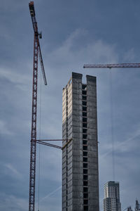 Low angle view of crane by building against sky