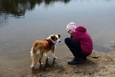 Smiling girl crouching by dog at lakeshore