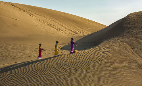 Women carrying containers while walking on sand dunes in desert