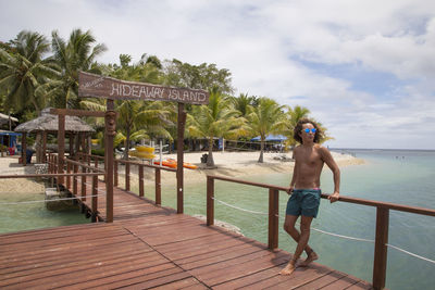 Man standing on railing by sea against sky