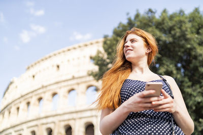Delighted female traveler using smartphone outside famous attraction