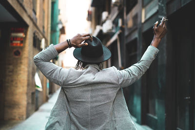 Rear view of man with arm raised holding cigarette in city