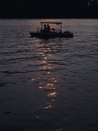 Silhouette people in boat against sky during sunset