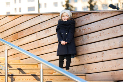 A 5-year-old girl stands on a wooden ladder.