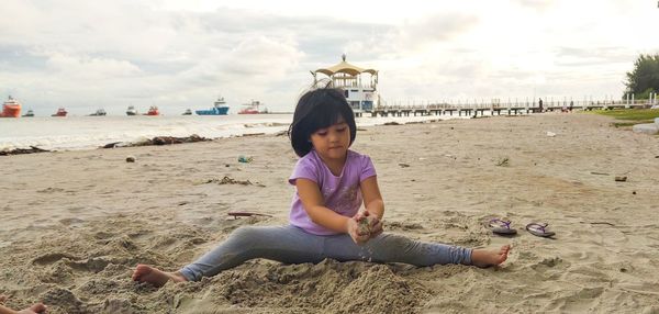 Full length of boy sitting on sand at beach against sky