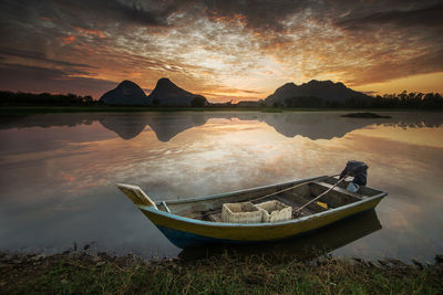 Boat moored in lake against sky during sunset