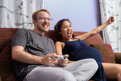 Cheerful man playing game with pregnant wife at home