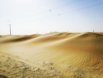 Low angle view of electricity pylon on sand against sky during sunny day